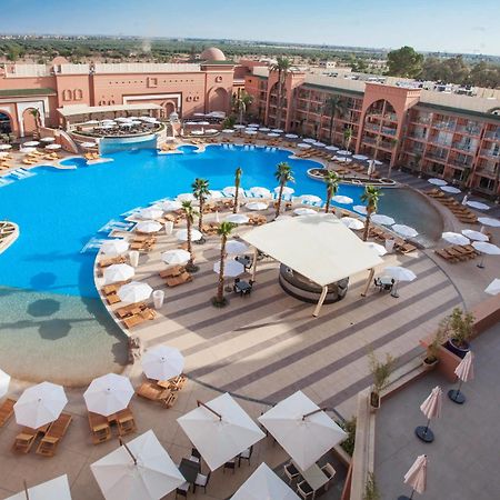 Savoy Le Grand Hotel Marrakech Марракеш Екстер'єр фото The photo shows a large, luxurious hotel resort with a spacious swimming pool at its center. The pool area features several lounge chairs and umbrellas arranged around the water, providing a relaxing atmosphere for guests. Surrounding the pool are la